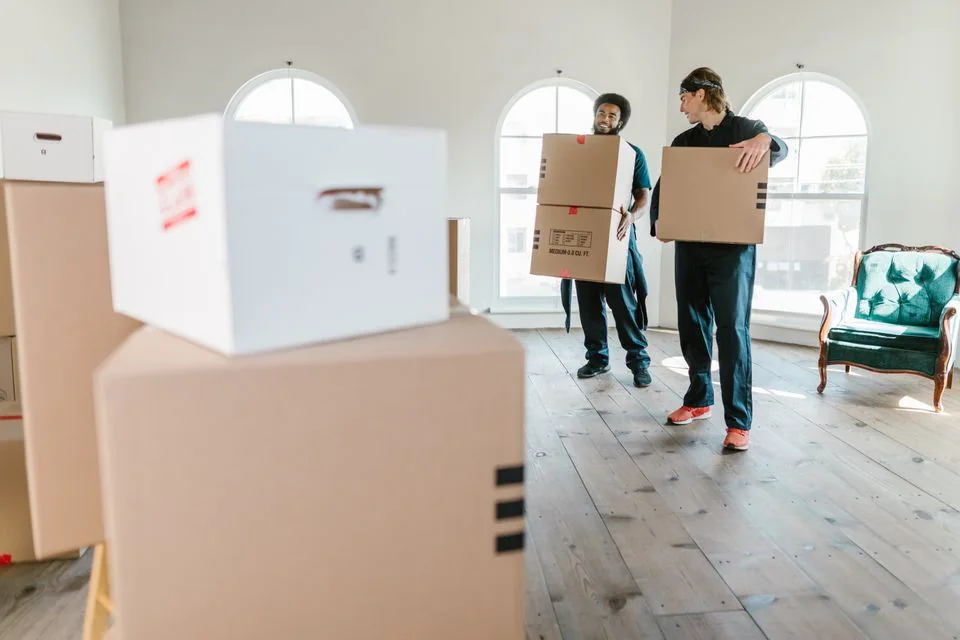 Two movers carrying packed boxes into a home.