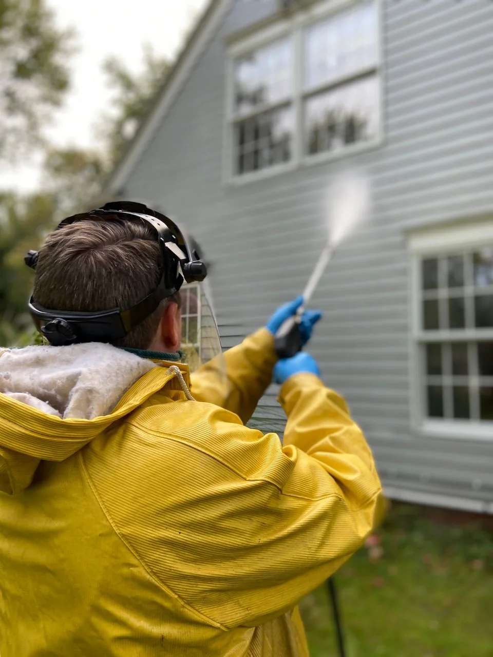 Worker in protective gear pressure washing house siding.
